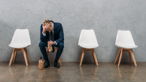 Lonely businessman drinking alcohol while sitting on chair under concrete wall