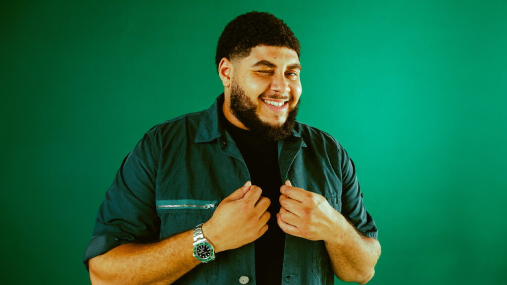 Big Zuu winking at the camera with a green background (Credit - Sharmarke Abdi)