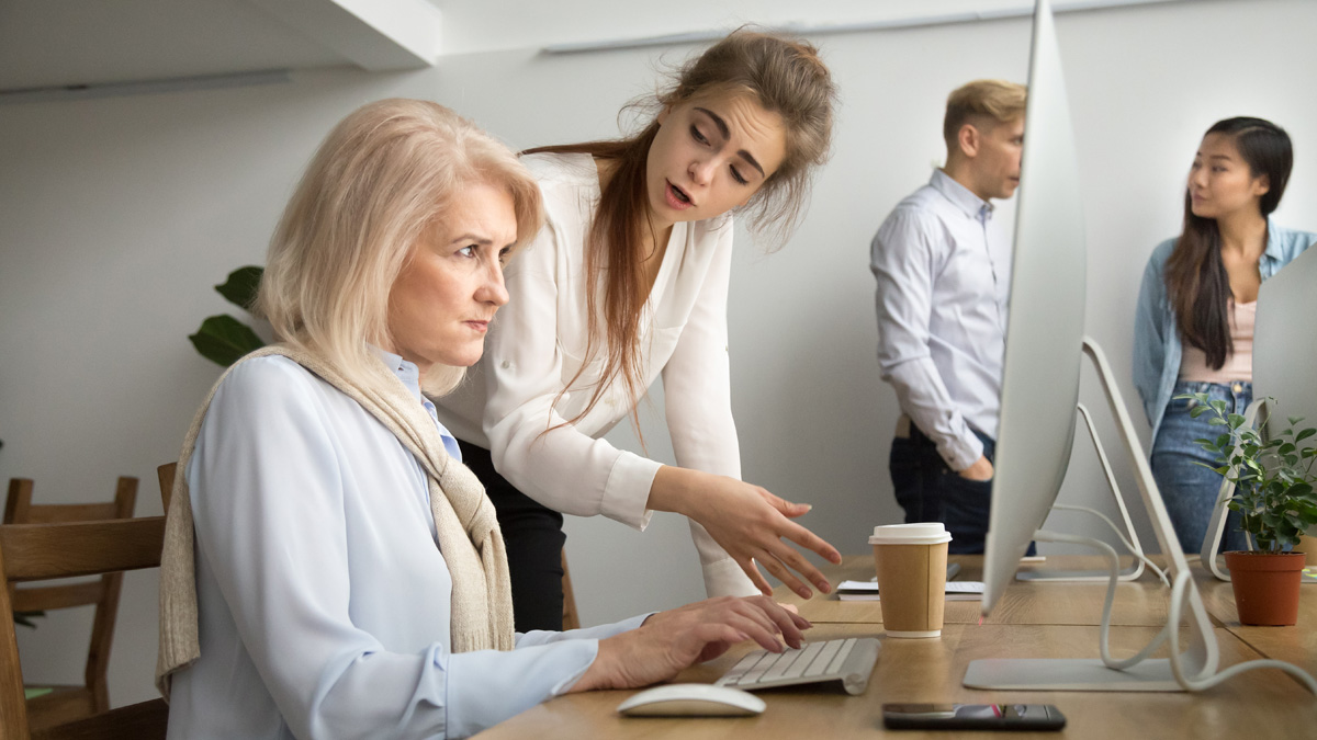 Young team leader correcting offended senior employee working on computer in office